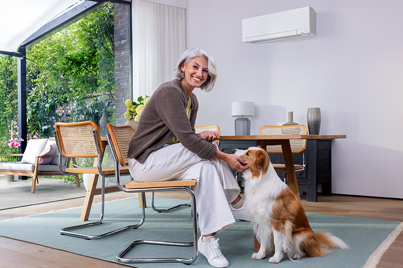 Vrouw zit in woonkamer met hond en lucht-lucht warmtepomp